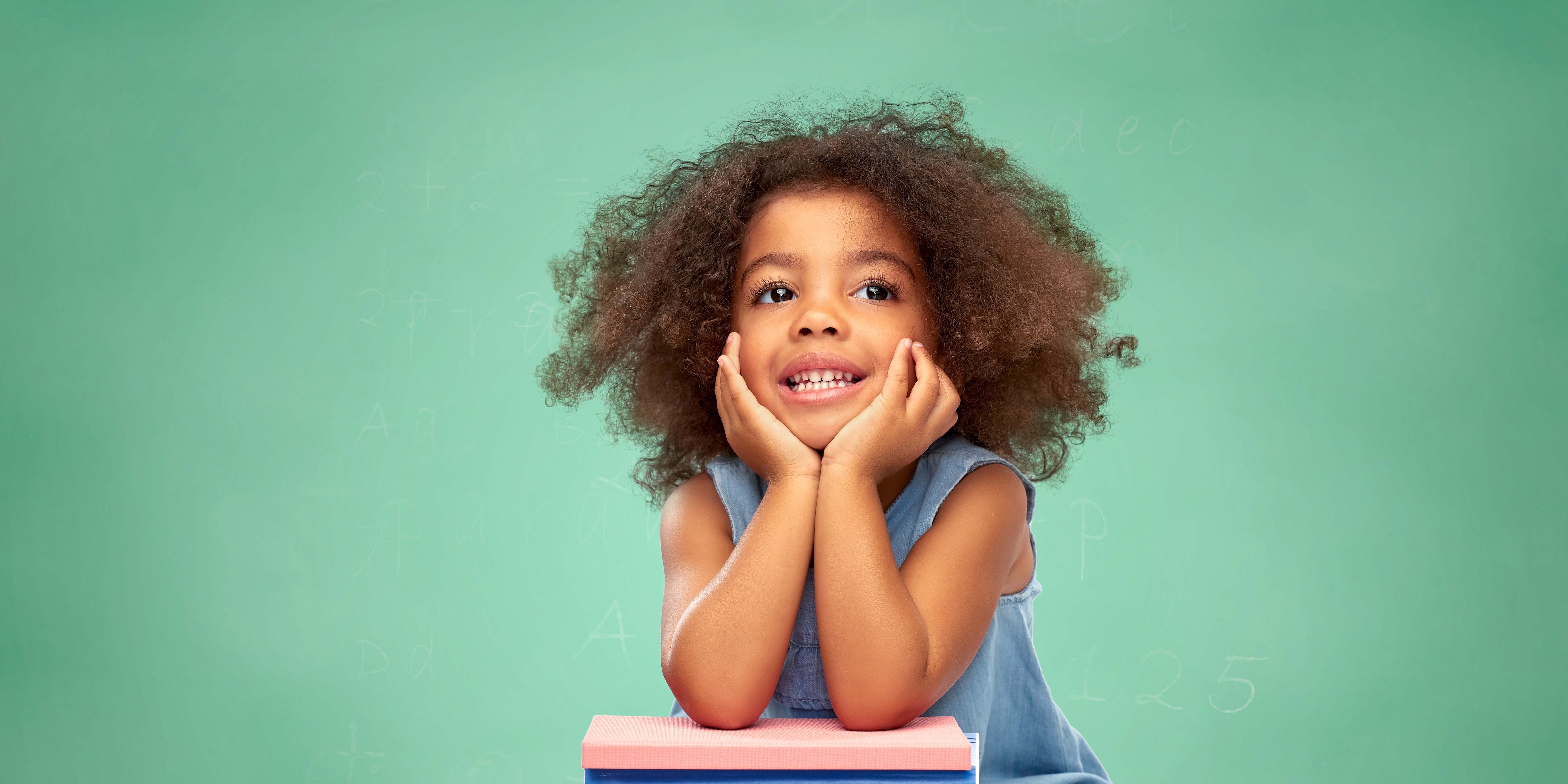 A preschool girl is sitting with her face resting on her folded hands