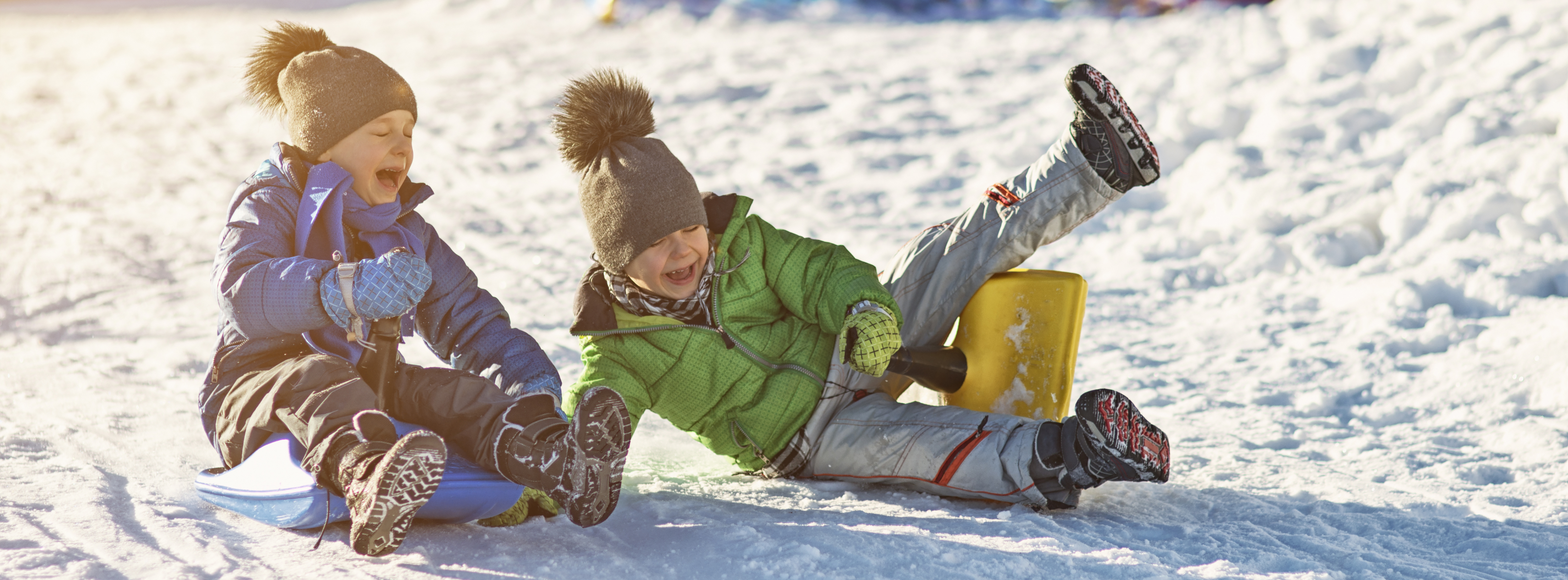 Two preschool children are sliding down the hill in the winter time