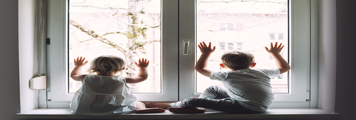 Two children are sitting on the window ledge, looking outside